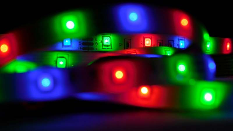 Modern living room illuminated by multicolored RGB strip lights under cabinets and behind TV